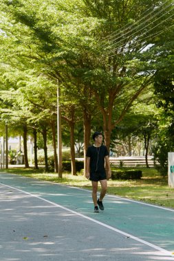 Yakışıklı, genç Asyalı erkek sporcu. Akıllı telefonuyla antrenman müziği dinliyor. Spor kıyafetleri giyiyor, konsept dışında koşuyor.