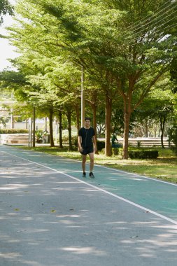 Yakışıklı, genç Asyalı erkek sporcu. Akıllı telefonuyla antrenman müziği dinliyor. Spor kıyafetleri giyiyor, konsept dışında koşuyor.