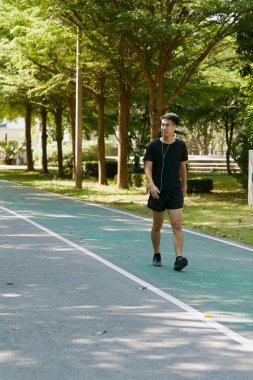 Yakışıklı, genç Asyalı erkek sporcu. Akıllı telefonuyla antrenman müziği dinliyor. Spor kıyafetleri giyiyor, konsept dışında koşuyor.