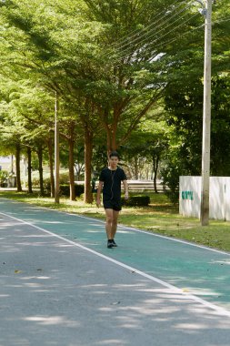 Yakışıklı, genç Asyalı erkek sporcu. Akıllı telefonuyla antrenman müziği dinliyor. Spor kıyafetleri giyiyor, konsept dışında koşuyor.