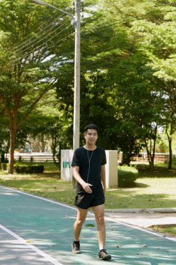 Yakışıklı, genç Asyalı erkek sporcu. Akıllı telefonuyla antrenman müziği dinliyor. Spor kıyafetleri giyiyor, konsept dışında koşuyor.