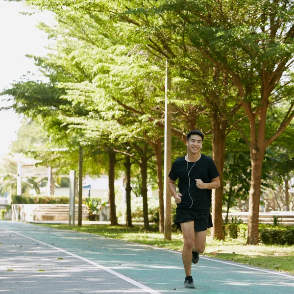 Yakışıklı Asyalı genç bir sporcunun portresi. Koşu yapıyor. Akıllı telefon konseptiyle müzik dinliyor.