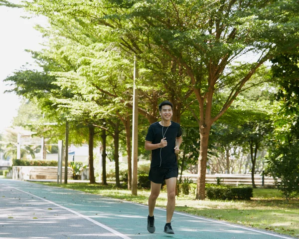 Yakışıklı Asyalı genç bir sporcunun portresi. Koşu yapıyor. Akıllı telefon konseptiyle müzik dinliyor.