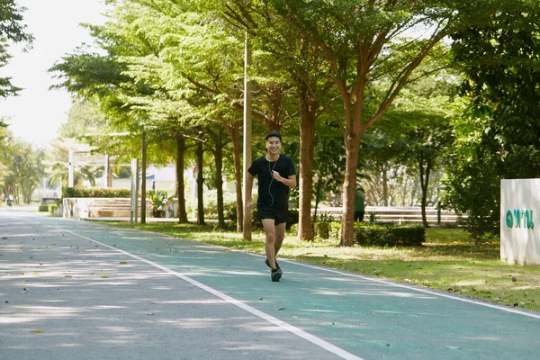 Yakışıklı Asyalı genç bir sporcunun portresi. Koşu yapıyor. Akıllı telefon konseptiyle müzik dinliyor.
