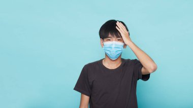 Mavi yalıtılmış arka plan, Coronavirus konsepti üzerinde Coperid-19 'a karşı yüz maskesi takan Asyalı genç adama yakın çekim.
