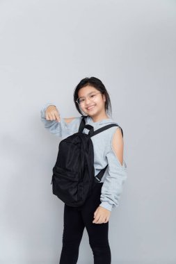Sırt çantalı mutlu güzel bir kızın portresi kolları kapalı gri arka planda duruyor, okula geri dönüyor..