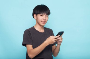 Genç Asyalı adam mavi arkaplan ile izole akıllı telefon kullanıyor