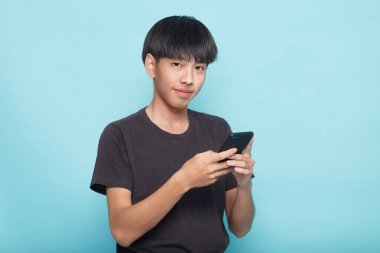 Genç Asyalı adam mavi arkaplan ile izole akıllı telefon kullanıyor