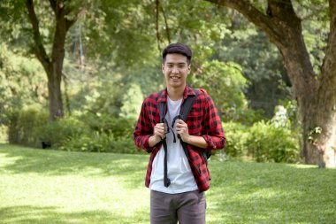 Yeşil ormanda sırt çantası taşıyan yakışıklı ve mutlu bir turist.