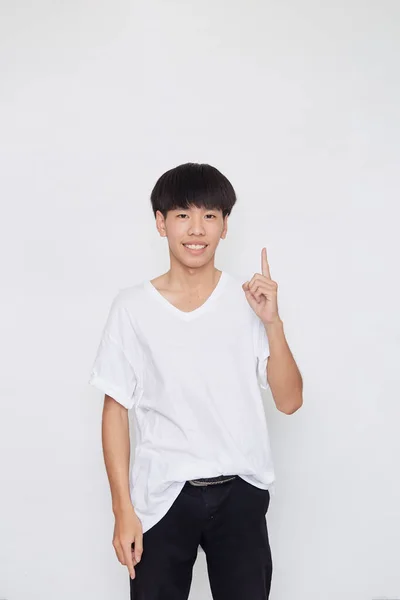 一个笑容满面的亚洲男人穿着随意的白色T恤 手指着白色背景旁边空旷的空间的画像 — 图库照片