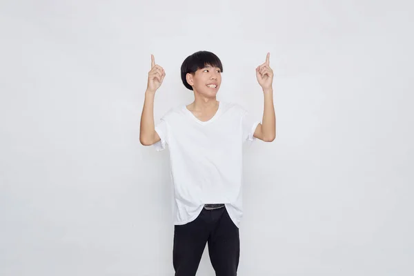 幸せな笑顔の肖像白い背景に空のスペースに手を指すカジュアルな白いTシャツを着てアジアの男 — ストック写真