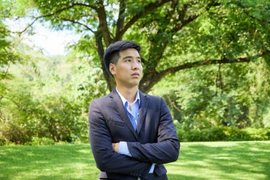 Genç bir Asyalı işadamı doğa parkında dinleniyor.