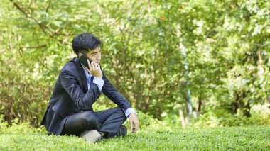 Genç bir Asyalı işadamı doğa parkında dinleniyor.