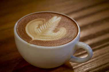 Yüzeyinde süt sanatı olan bir fincan sıcak kahve, ahşap masaya konur.