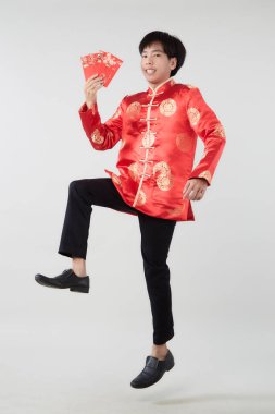 Yeni yıl konsepti için açık gri izole stüdyo arka planında kırmızı zarflar taşıyan, doğulu yakışıklı Asyalı adamın zıplayan portresi.