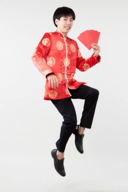 Yeni yıl konsepti için açık gri izole stüdyo arka planında kırmızı zarflar taşıyan, doğulu yakışıklı Asyalı adamın zıplayan portresi.