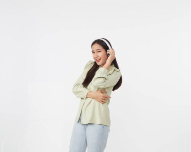 Neşeli, güzel, Asyalı bir kadın dans ediyor, beyaz arka planda kablosuz kulaklıkla müzik dinliyor.