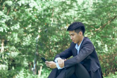 Parkta oturan yakışıklı bir Asyalı iş adamı.