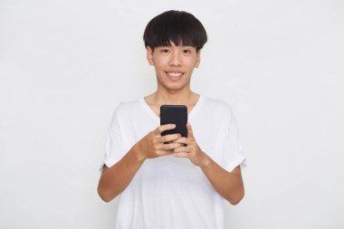 Yakışıklı Asyalı erkek öğrenci arka planda akıllı telefon kullanarak mesajlar yolluyor. Boşluk ve maketi kopyala