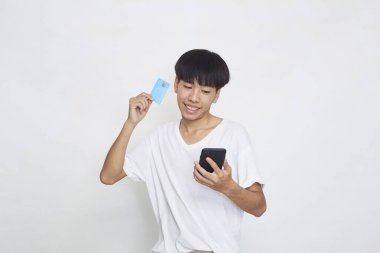 Cep telefonu tutan ve kredi kartını gösteren yakışıklı Asyalı genç bir adamın portresi.