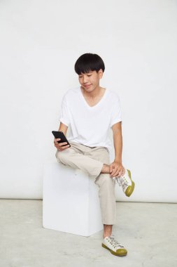 Yakışıklı Asyalı adam beyaz arka planda izole edilmiş telefonu kullanıyor. Boşluğu kopyala