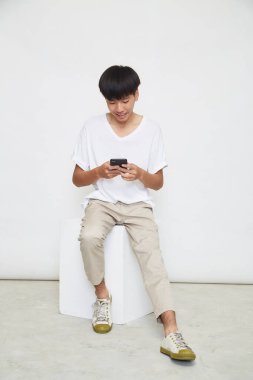 Yakışıklı Asyalı adam beyaz arka planda izole edilmiş telefonu kullanıyor. Boşluğu kopyala