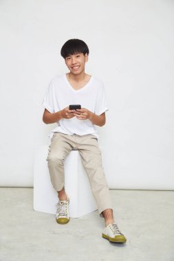 Yakışıklı Asyalı adam beyaz arka planda izole edilmiş telefonu kullanıyor. Boşluğu kopyala