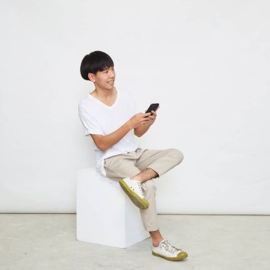 Yakışıklı Asyalı adam beyaz arka planda izole edilmiş telefonu kullanıyor. Boşluğu kopyala