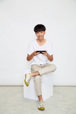 Yakışıklı Asyalı adam beyaz arka planda izole edilmiş telefonu kullanıyor. Boşluğu kopyala