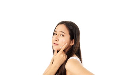 Yanaklarında nemlendirici kullanan bir modelin yakın çekimi. Bir kadın yüzüne nemlendirici krem sürüyor. Güzel bir kızın güzel bir yüz teni vardır. Cilt bakımı. beyaz arkaplan