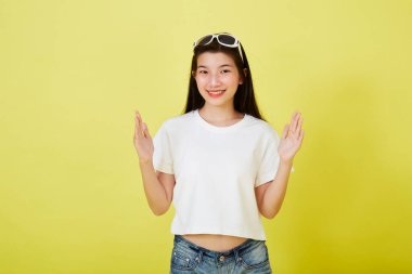 Genç ve güzel Asyalı kadın gülümseyip izole edilmiş sarı renkli arka planı işaret ediyor.