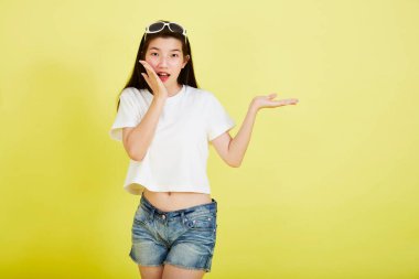 Genç ve güzel Asyalı kadın gülümseyip izole edilmiş sarı renkli arka planı işaret ediyor.