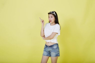 Genç ve güzel Asyalı kadın gülümseyip izole edilmiş sarı renkli arka planı işaret ediyor.