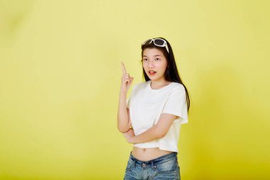 Genç ve güzel Asyalı kadın gülümseyip izole edilmiş sarı renkli arka planı işaret ediyor.