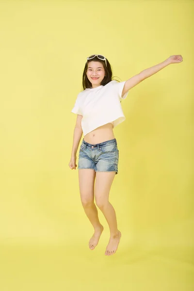 かなり若いですアジアの女の子の肖像幸せとジャンプで空中で明るい黄色の背景 — ストック写真
