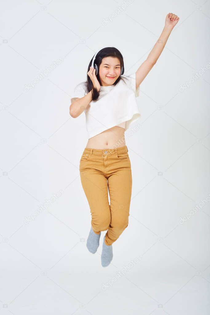 young Asian woman with headphones and jumping on color background