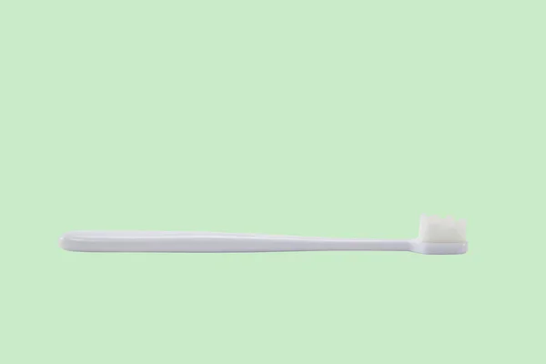 緑の背景に白い毛を持つ白いプラスチック製の歯ブラシ — ストック写真