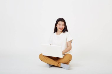 Dizüstü bilgisayarda çalışan gülümseyen Asyalı kadın bacak bacak bacak üstüne atarak yerde oturuyor.