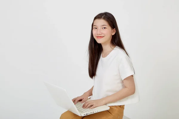 快乐迷人的年轻女性 带着笔记本电脑 盘腿坐着 在白色的工作室背景下看着空旷的空间 — 图库照片