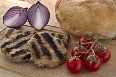 ızgara köfte kiraz domatesleri, ekmek ve ahşap tabakta kırmızı soğan.