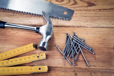 Tahta arka planda testere, çekiç, çivi ve katlanan cetvel.
