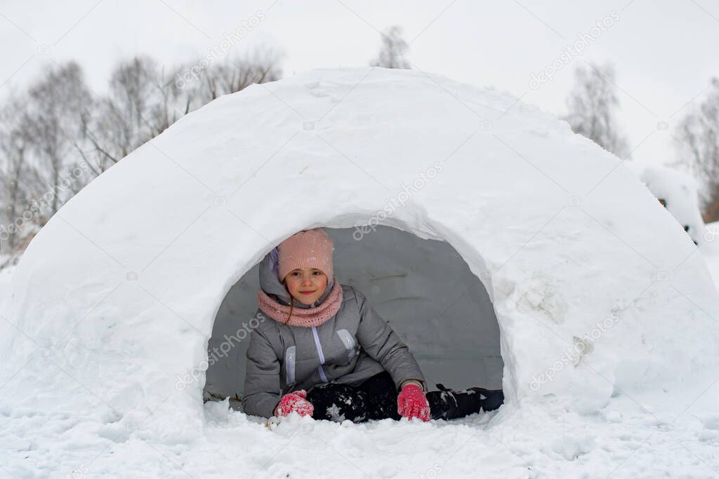 girl in winter clothes lying on the snow near the entrance to igloo