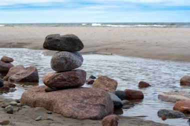 Kumsalda istiflenmiş deniz taşları. Arka planda karamsar bulutlar ve deniz suyu