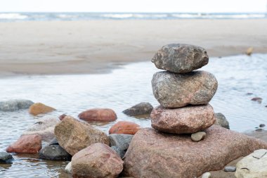 Kumsalda istiflenmiş deniz taşları. Arka planda karamsar bulutlar ve deniz suyu