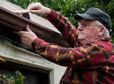 senior male cleaning out gutter outside house