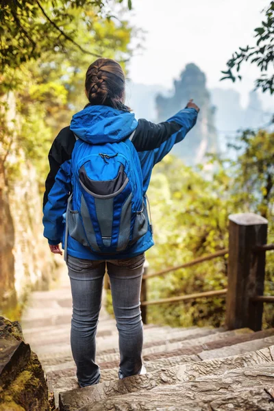 Giovane turista donna con zaino blu che punta verso le montagne — Foto Stock