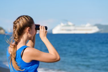 Young female tourist looking through binoculars at cruise ship