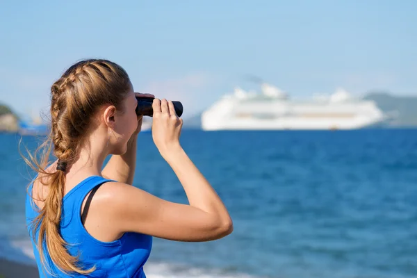 Young female tourist looking through binoculars at cruise ship — 图库照片