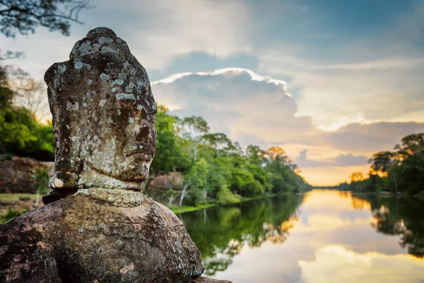 Mechový kamenná tvář Asura a slunce nad příkopem. Angkor, Kambodža — Stock fotografie