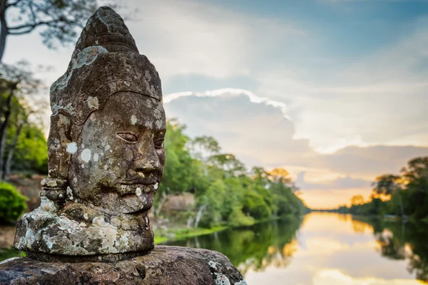 Mossy kamenná tvář Asura a západ slunce nad příkop v Angkor, Kambodža — Stock fotografie